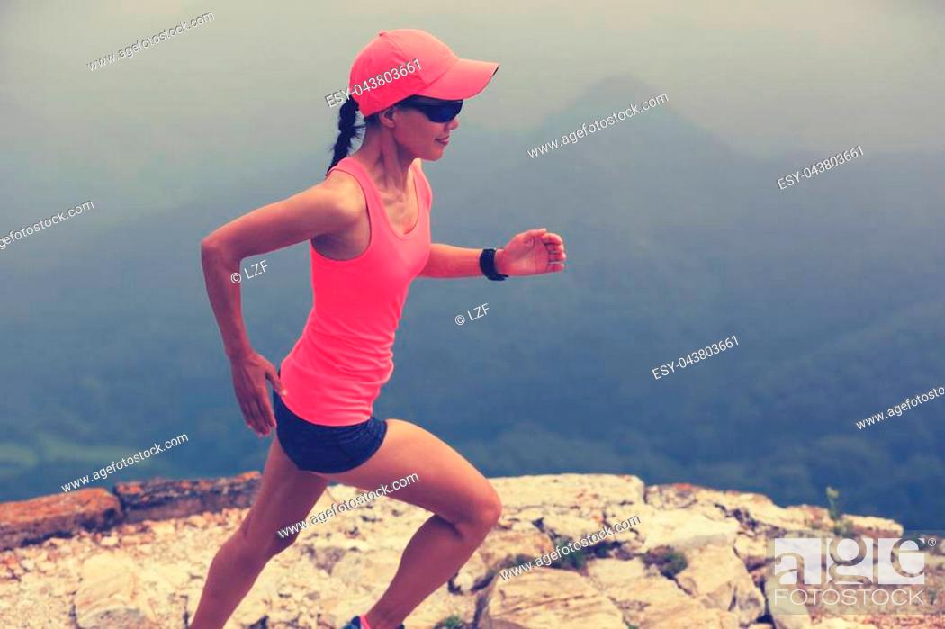 Stock Photo: young woman trail runner running on great wall on the top of mountain.