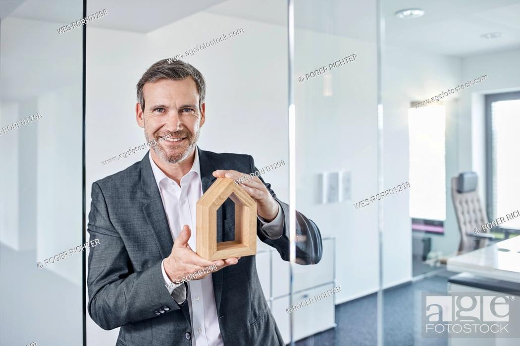 Imagen: Portrait of smiling businessman holding architectural model in office.