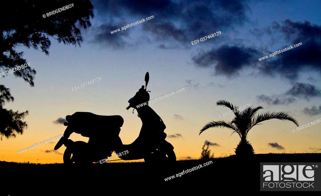 Stock Photo: A scooter sillouetted against a sunset sky, wth a pinapple palm next to it.