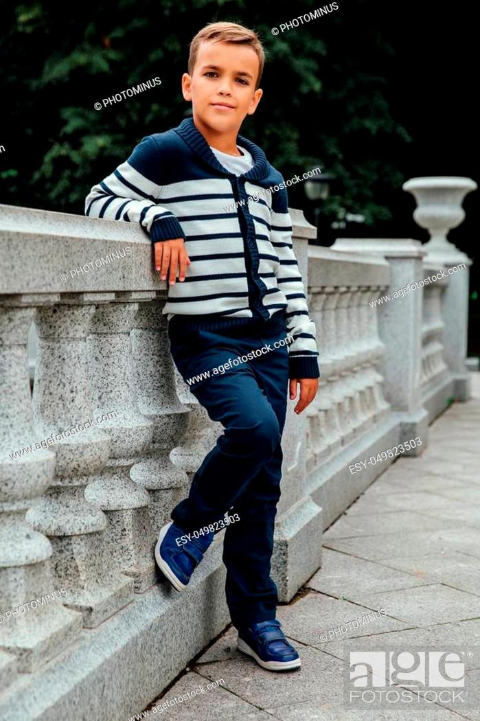 Stock Photo: Stylish rich little boy in fashionable clothes. Leaned on Granite-stone handrails. stylish, handsome posing outside in the city park.