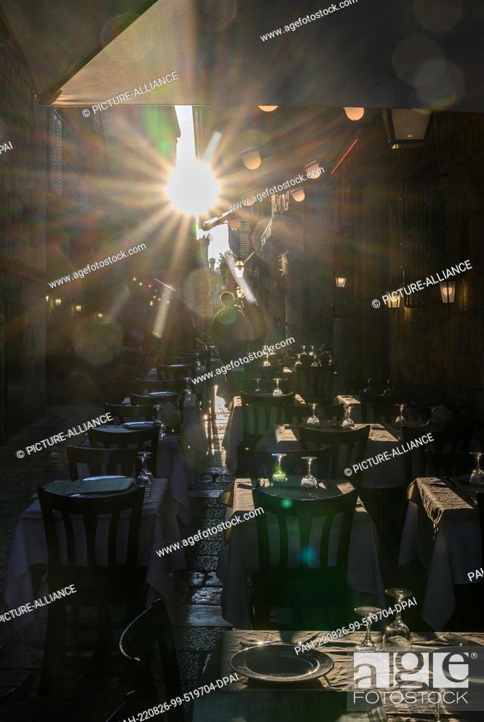 Stock Photo: 14 August 2022, Croatia, Dubrovnik: The light of the setting sun is reflected in glasses placed on tables of a restaurant in the old town.