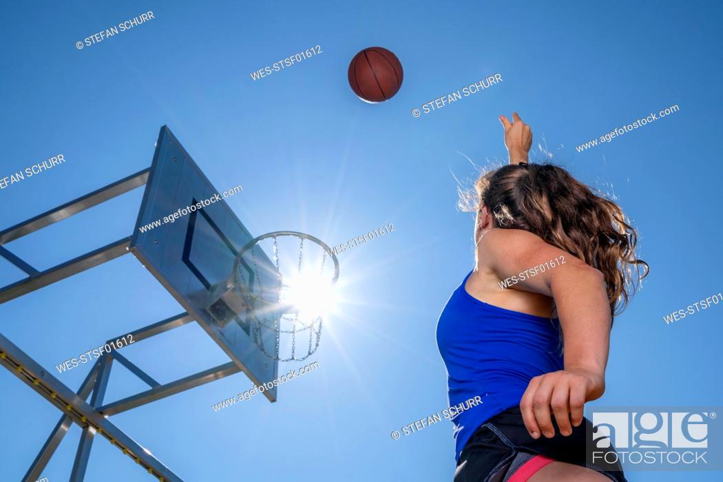 Stock Photo: Young woman playing basketball, against the sun.