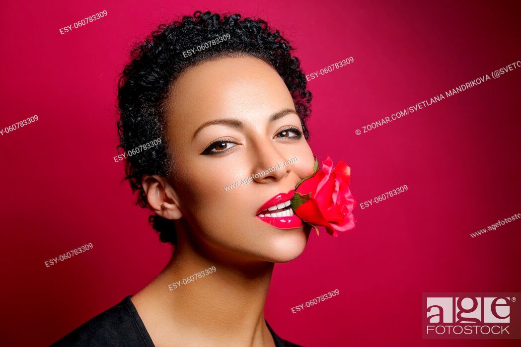 Stock Photo: beautiful young woman with red lips holding rose in mouth. studio beauty shot on dark red background. copy space.