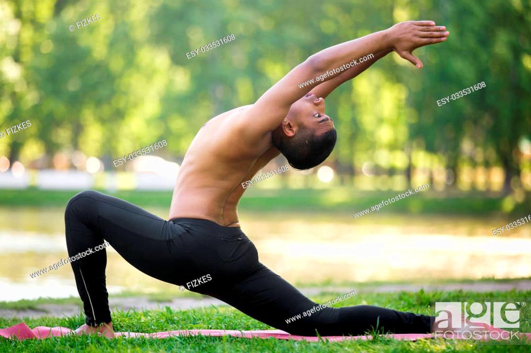 Stock Photo: Profile of sporty Indian young man practicing yoga, fitness, pilates on riverbank in park, doing low lunge exercise on river bank in park, full length.
