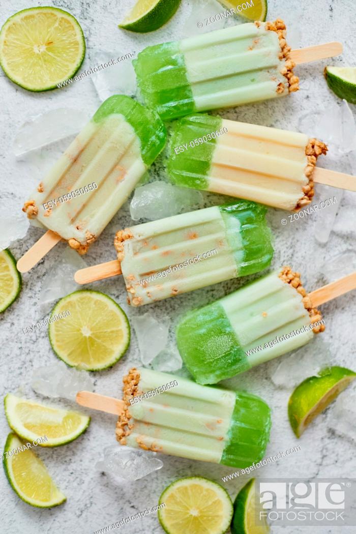 Stock Photo: Lime and cream homemade popsicles or ice creams placed with ice cubes on gray stone backdrop. Flat lay, top view.