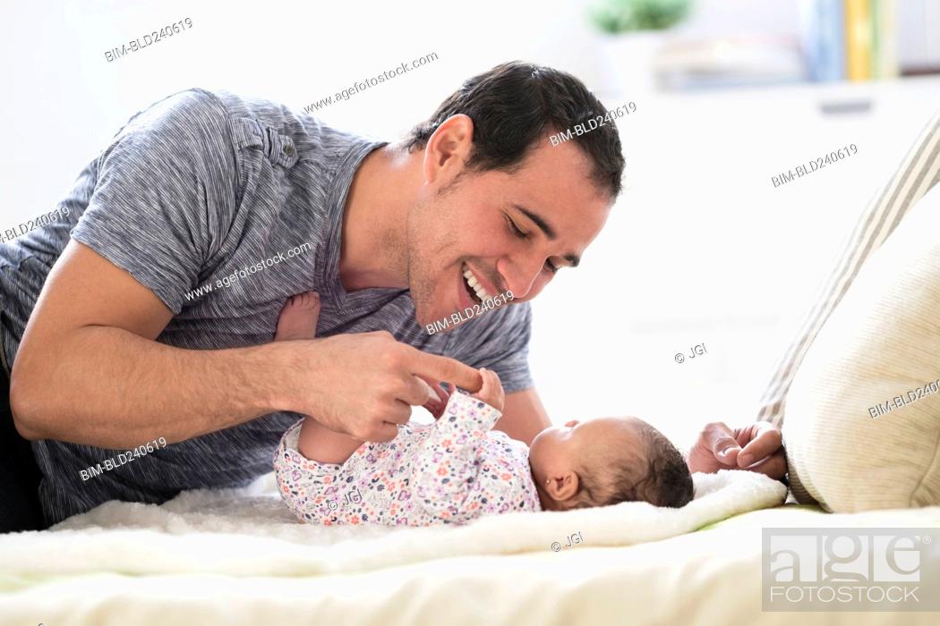 Photo de stock: Hispanic father laying on bed playing with baby daughter.