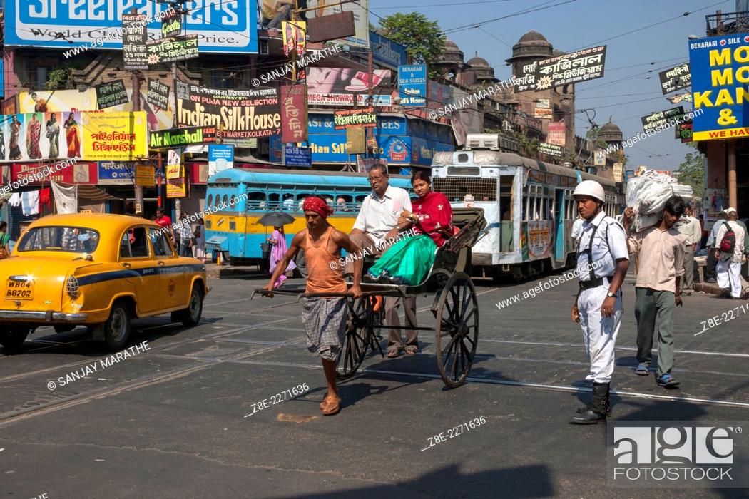 Stock Photo: A policemen looks on as a rickshaw puller ferries passengers amid yellow Ambassador taxis, trams and buses at a junction near college street in Kolkata.