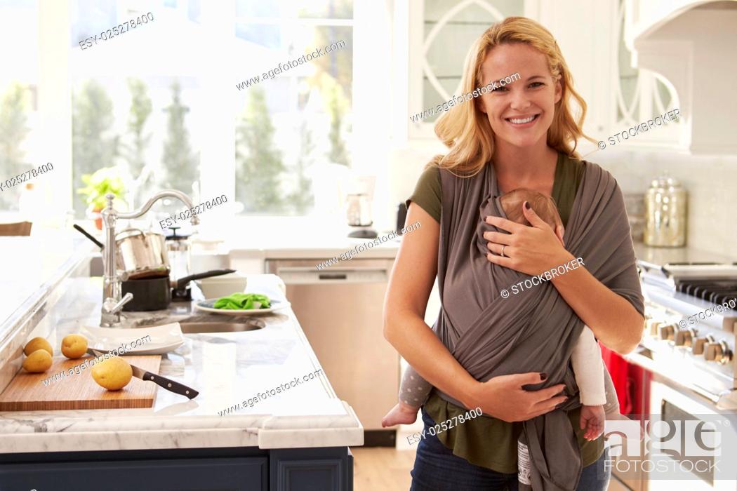 Stock Photo: Portrait Of Busy Mother With Baby In Sling At Home.