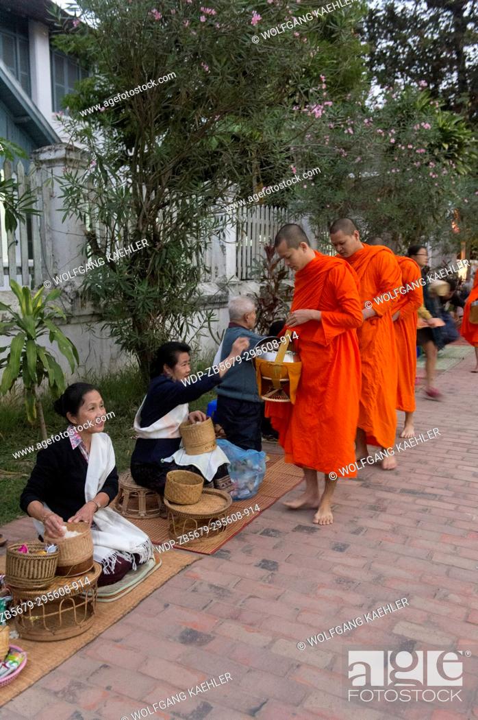Stock Photo: Buddhist monks receiving alms from the people early morning before sunrise in the UNESCO world heritage town of Luang Prabang in Central Laos.