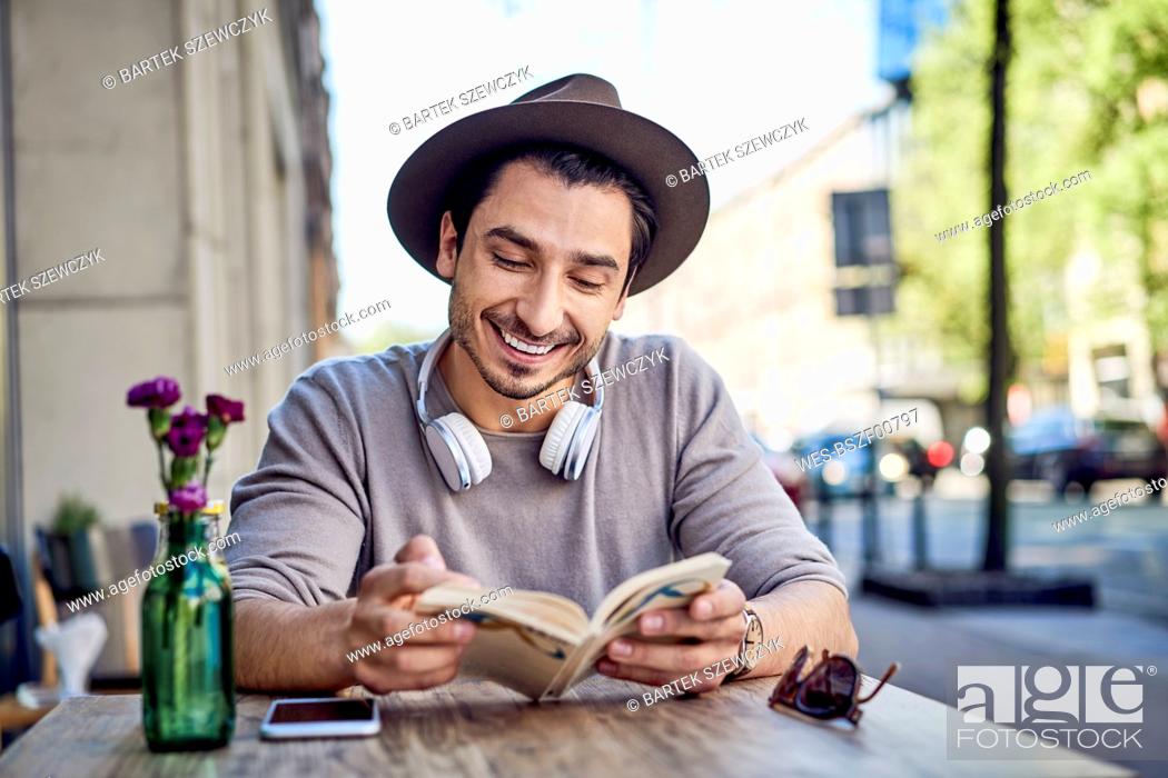 Stock Photo: Happy young man reading book at outdoors cafe.