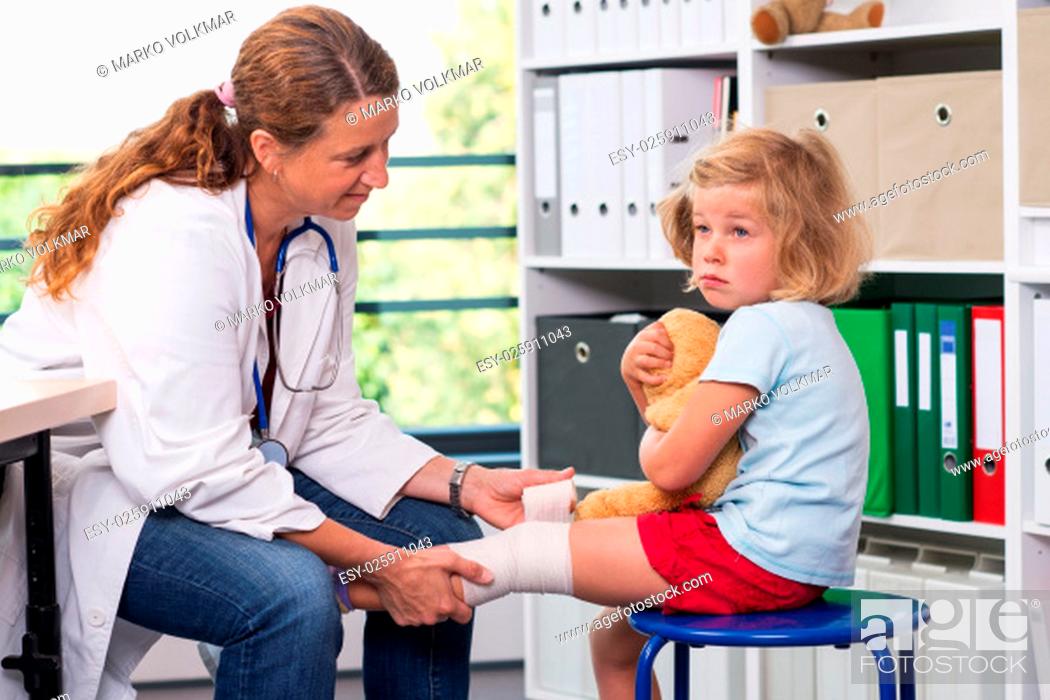 Stock Photo: female pediatrician in white lab coat bandaging the leg of a little girl.
