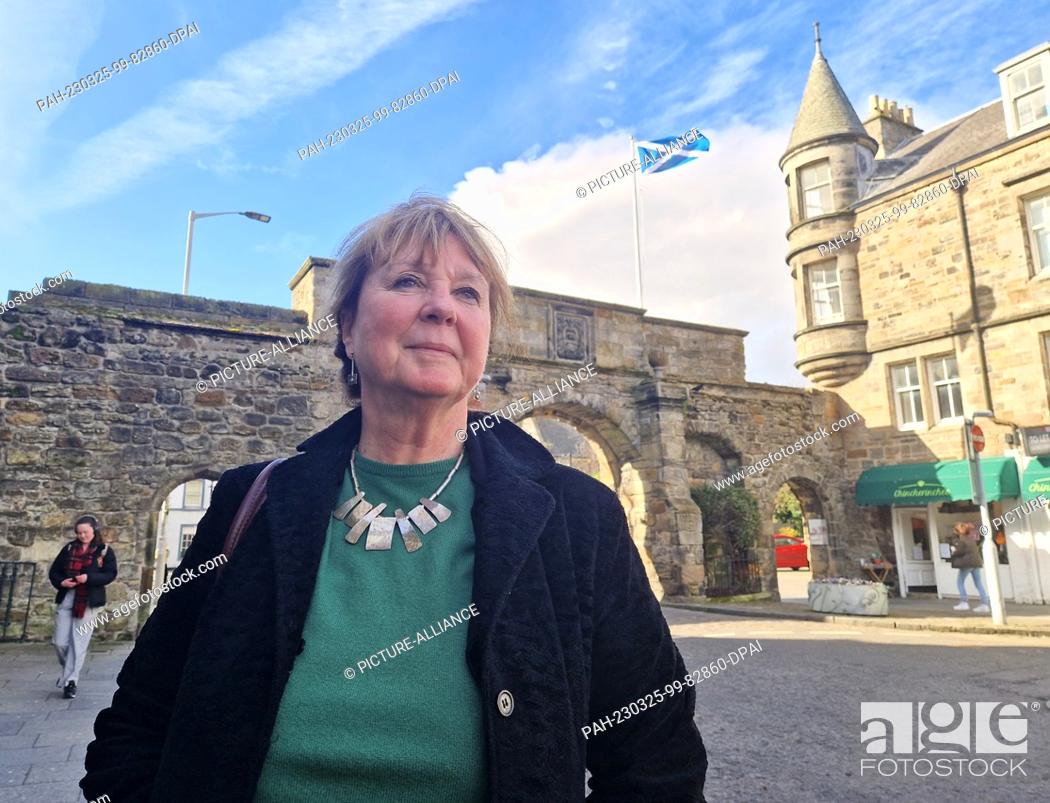 Stock Photo: 24 March 2023, Great Britain, St. Andrews: Independence activist Jane Philips from Dundee stands in front of an archway and a Scottish flag in the Scottish town.