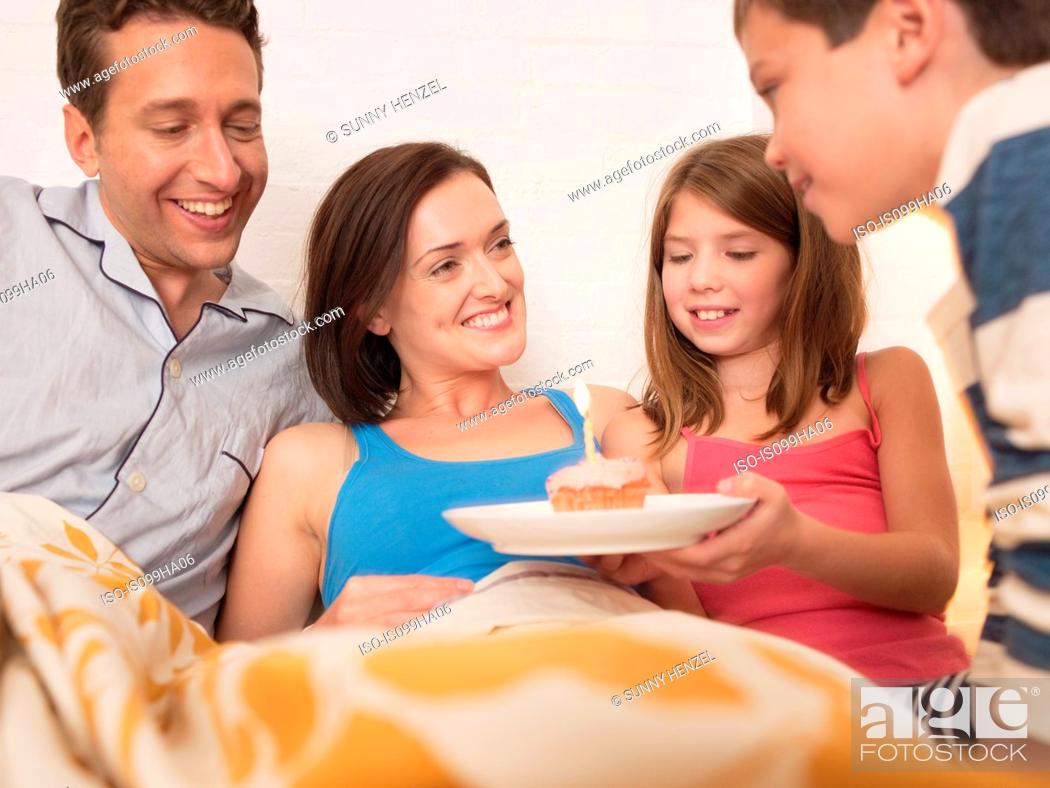 Stock Photo: Mid adult woman receiving birthday cake in bed from family.