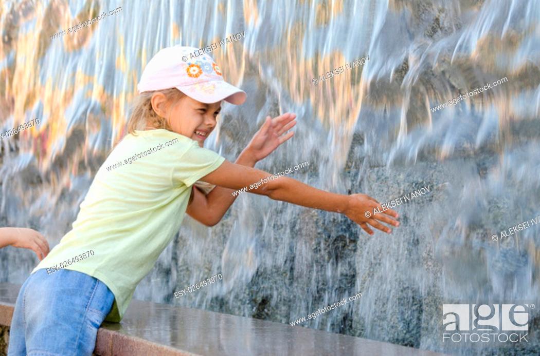 Stock Photo: Cheerful six year old girl in summer clothes hand trying to get the water artificial waterfall.