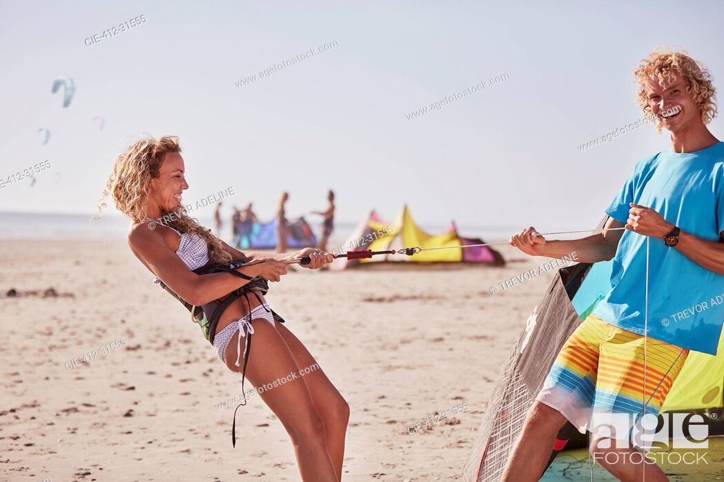 Photo de stock: Playful couple preparing kiteboarding equipment on sunny beach.
