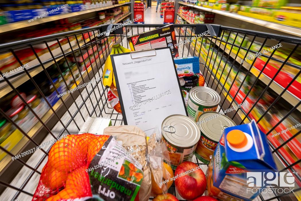 Stock Photo: 26 March 2020, Bavaria, Deggendorf: Food and a shopping list are in a shopping cart in a supermarket. Helpers provide food for the elderly and sick.