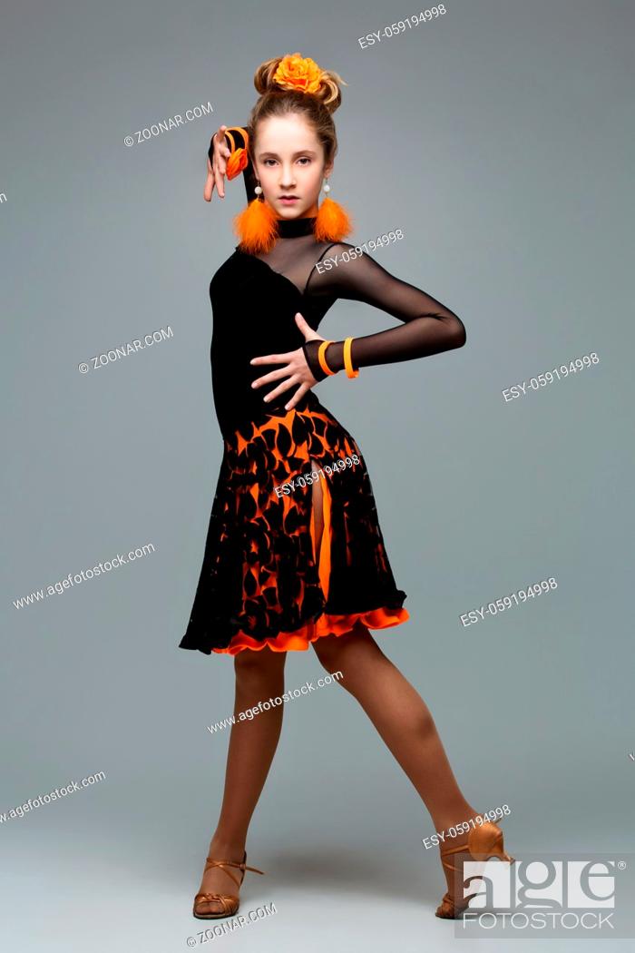Stock Photo: Beautiful teenage ballroom dancer girl in black and orange latina dress And accessories. Studio portrait on grey background. Copy space.