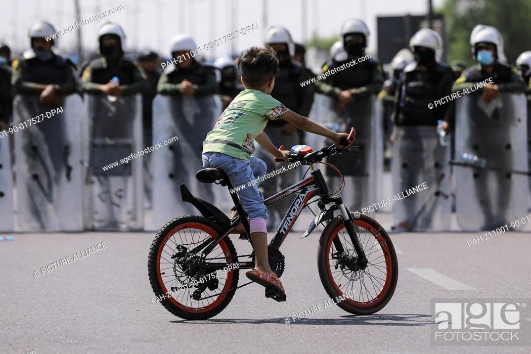 Stock Photo: 01 October 2021, Iraq, Baghdad: An Iraqi boy rides his bicycle in front of security forces officers during an anti-government march from Firdos Square to Tahrir.