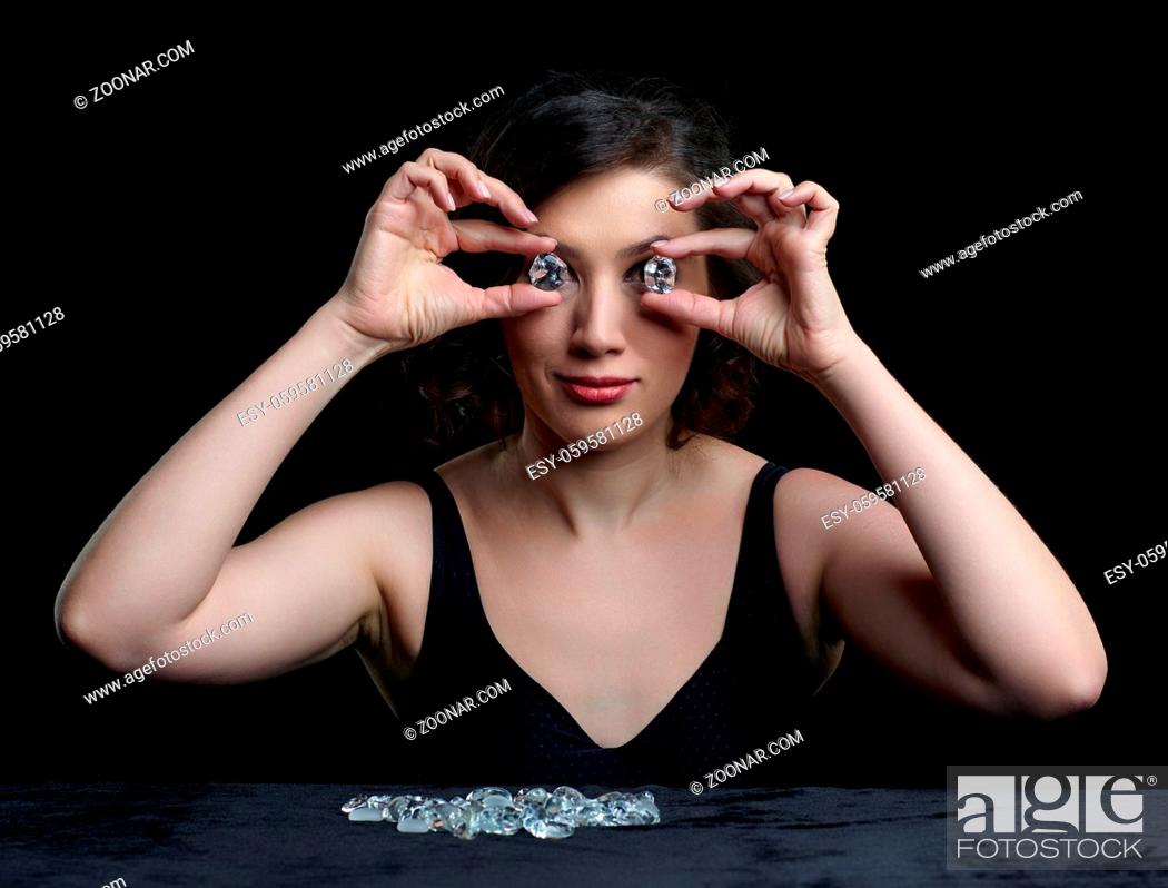 Stock Photo: Portrait of beautiful long-haired brunette woman on black background. Female sit at table covered by black velvet .and is looking through glass stone.