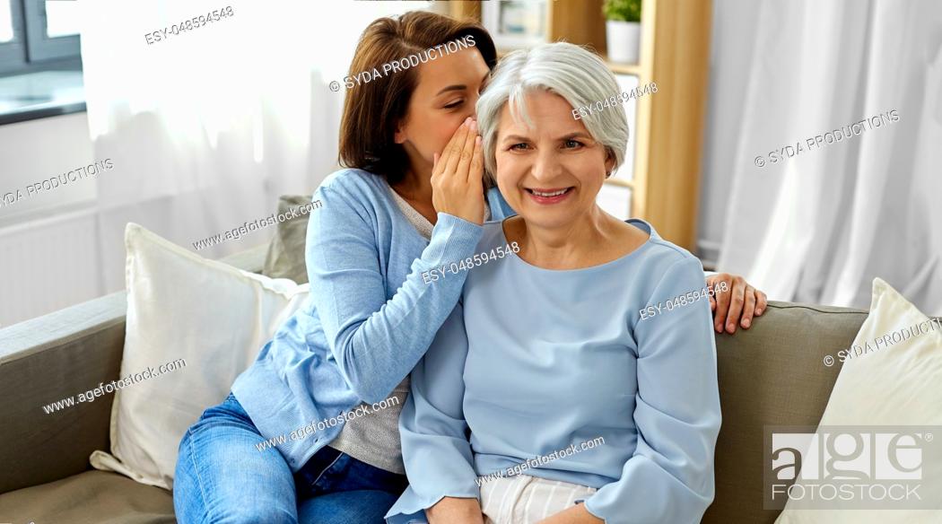 Stock Photo: adult daughter whispering to senior mother at home.