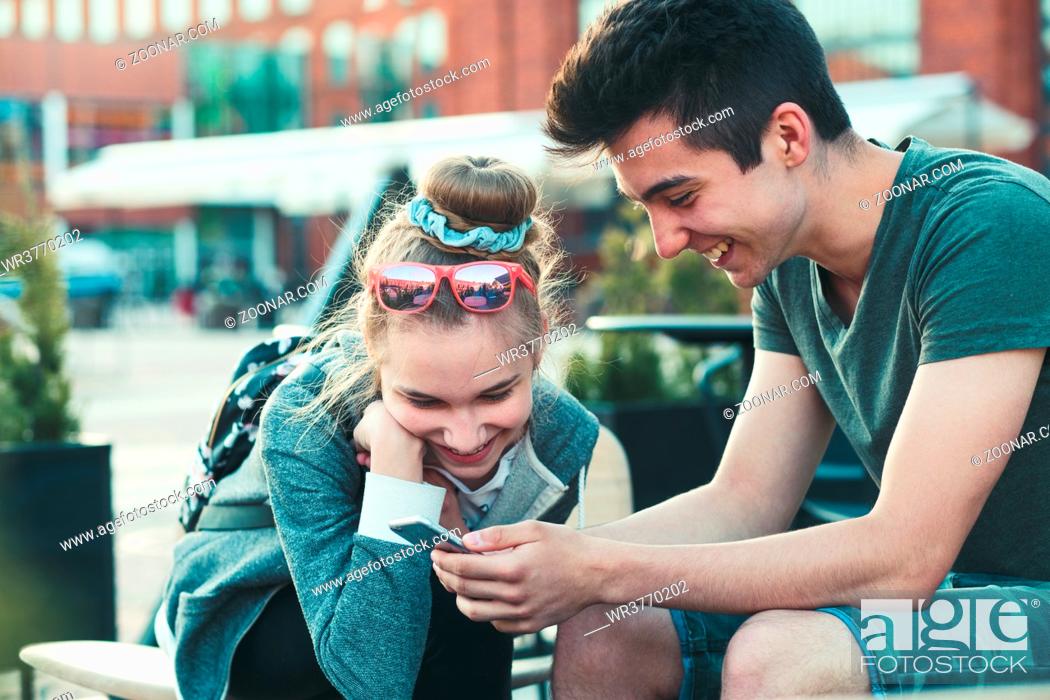 Stock Photo: Couple of friends, teenage girl and boy, having fun with smartphones, sitting in center of town, spending time together.