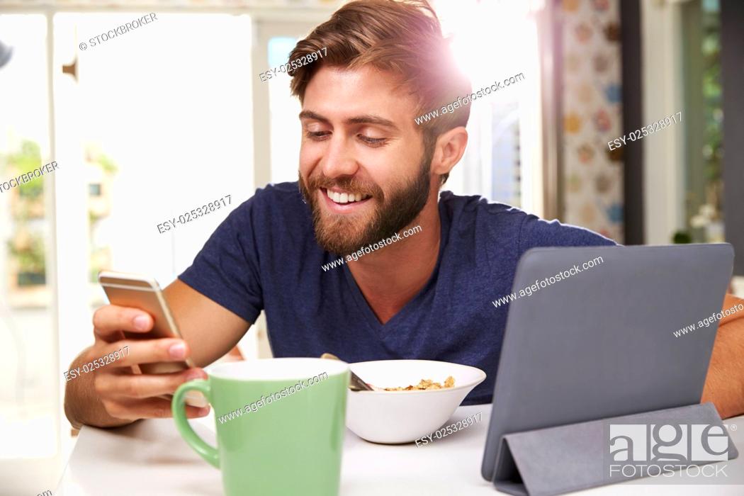 Stock Photo: Man Eating Breakfast Whilst Using Digital Tablet And Phone.