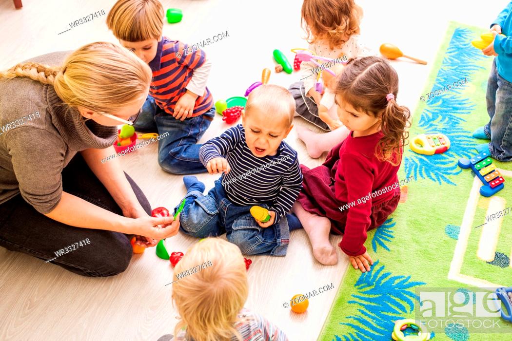 Stock Photo: Children with teacher in kindergarten playing cooks. Boy is crying and want a toy.