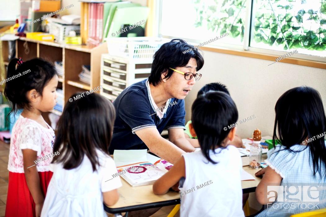 Stock Photo: Male teacher talking to group of children at a table n a Japanese preschool.