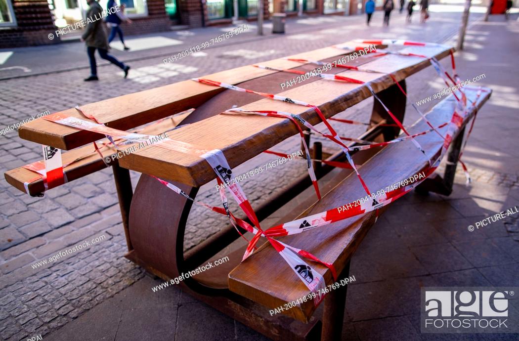 Stock Photo: 18 April 2020, Mecklenburg-Western Pomerania, Schwerin: A table wrapped with barrier tape in front of a snack bar in the pedestrian zone because of the corona.