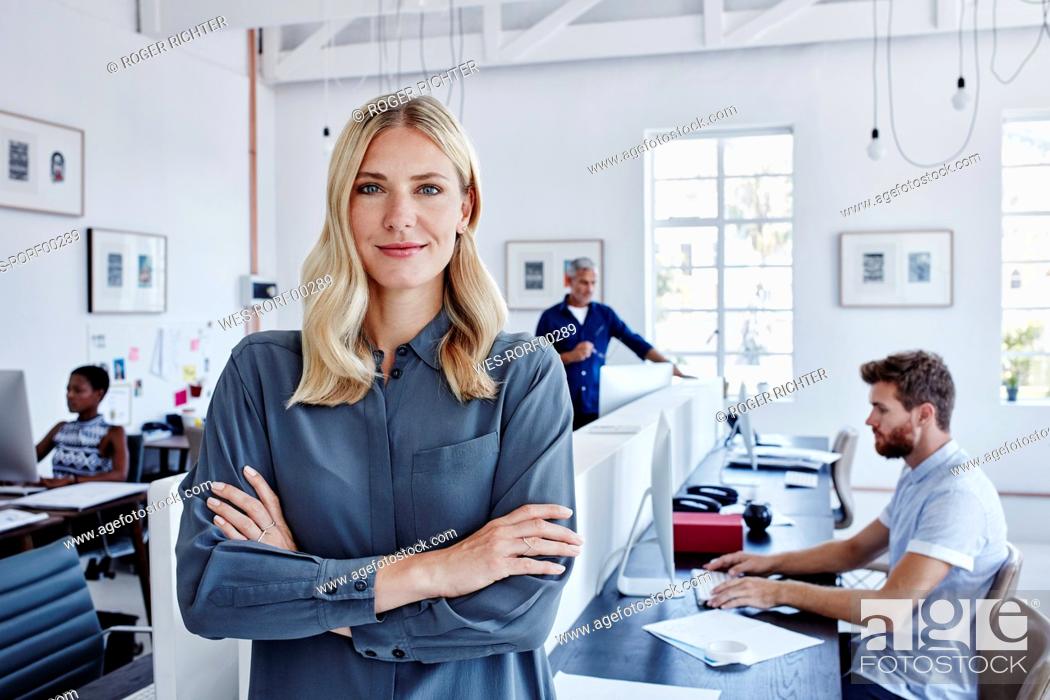 Stock Photo: Portrait of confident businesswoman in office with staff in background.