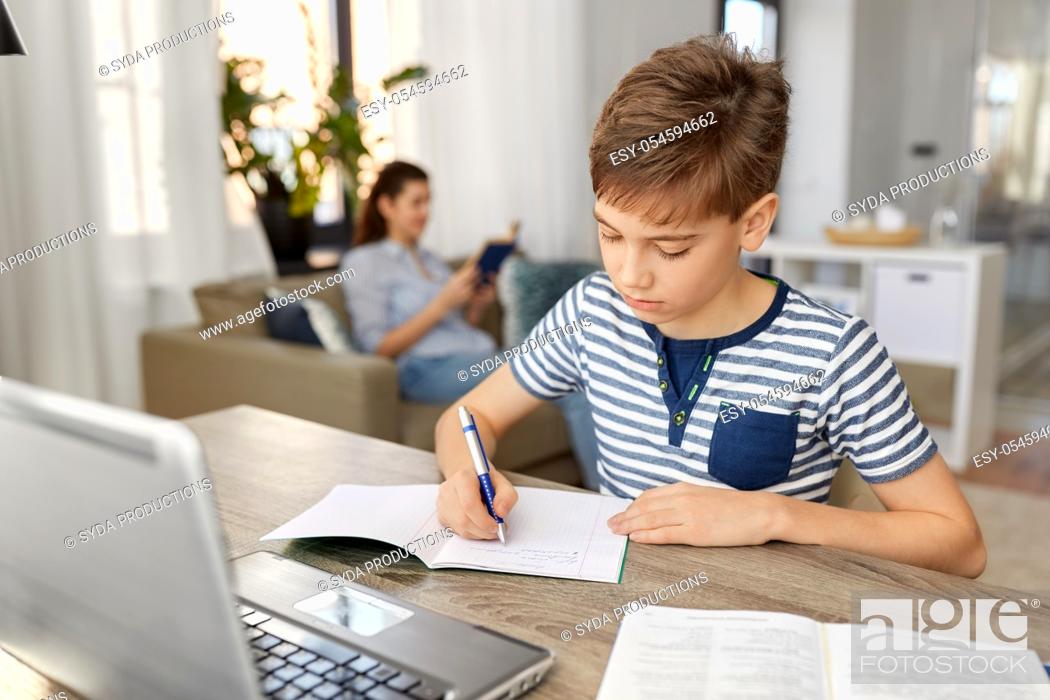 Stock Photo: student boy with book writing to notebook at home.