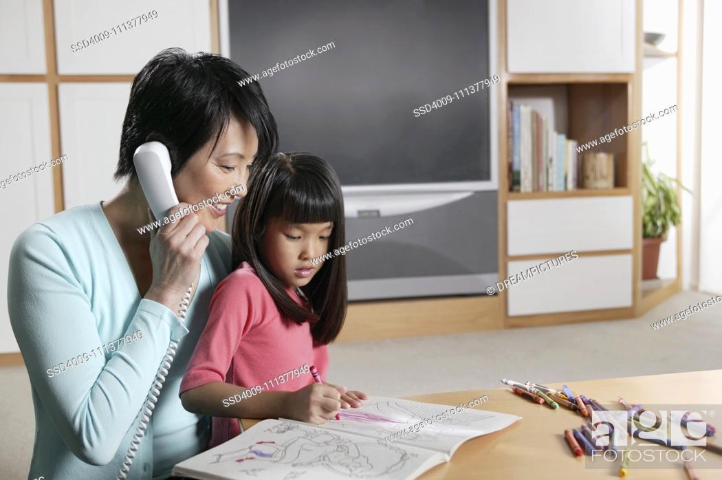 Stock Photo: Mother talking on the phone as her daughter draws.