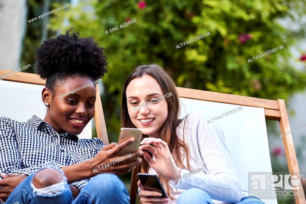 Photo de stock: Smiling young friends using smartphones in park.