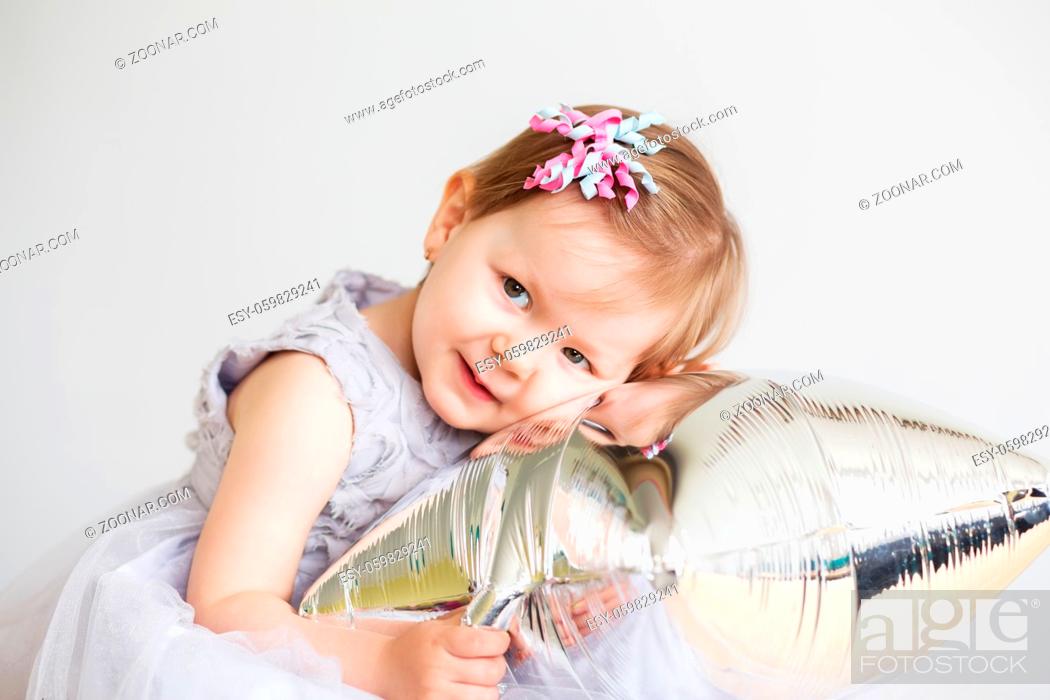 Stock Photo: Portrait of a lovely little girl in elegant gray dress in front of a white background. Little princess. Little baby girl playing with silver star-shaped balloon.
