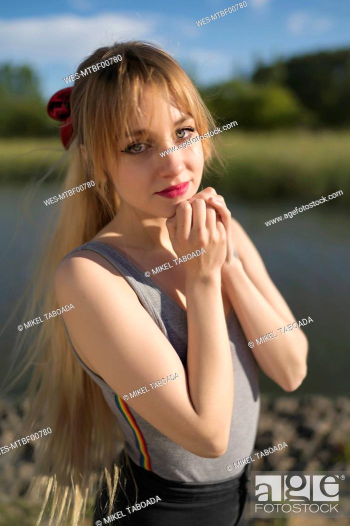 Stock Photo: Blond woman with hand on chin standing by lake.