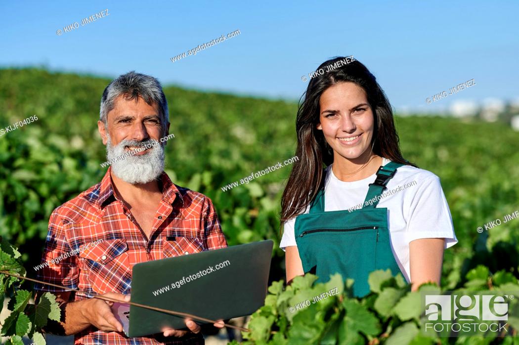 Stock Photo: Smiling male and female farmers standing amidst plants in vineyard on sunny day.