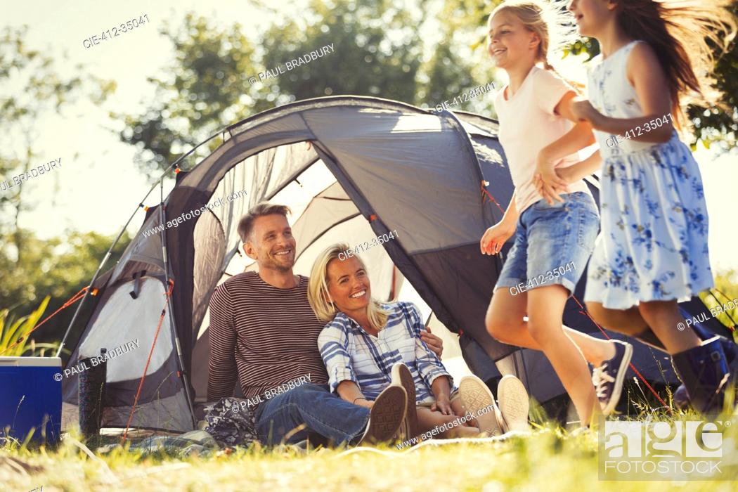 Stock Photo: Parents watching happy daughters running around sunny campsite tent.