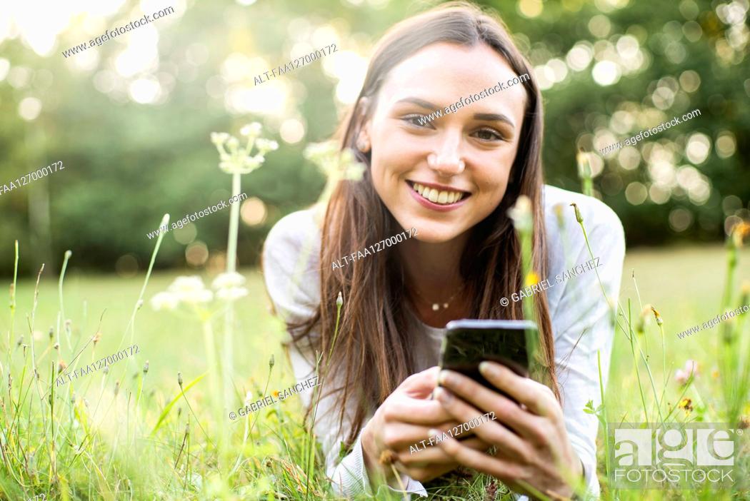 Stock Photo: Portrait of young woman using smart phone while lying in park.