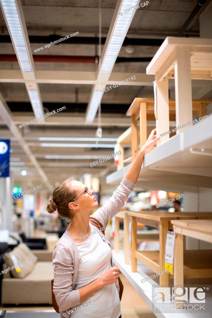 Stock Photo: Pretty, young woman choosing the right furniture for her apartment in a modern home furnishings store (color toned image; shallow DOF).