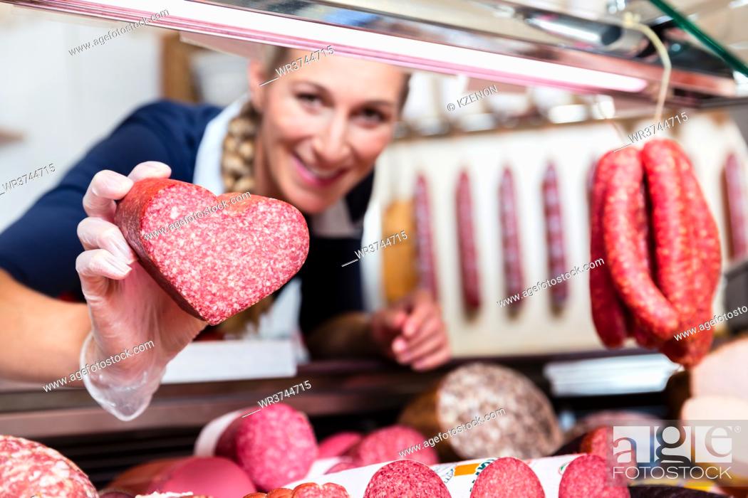 Stock Photo: Sales woman in meat shop showing a heart shaped sausage to customer.