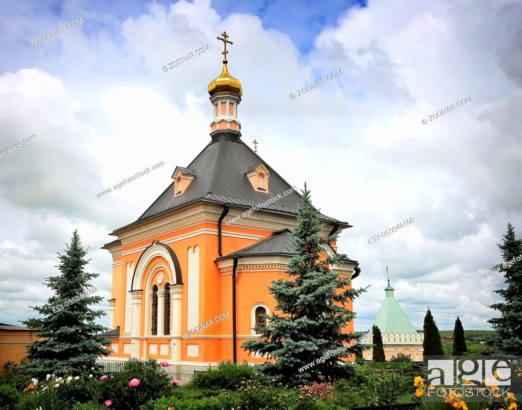 Imagen: A beautiful Orthodox temple located on a hill surrounded by flowers and plants: arborvitae, blue spruce, shrubs.
