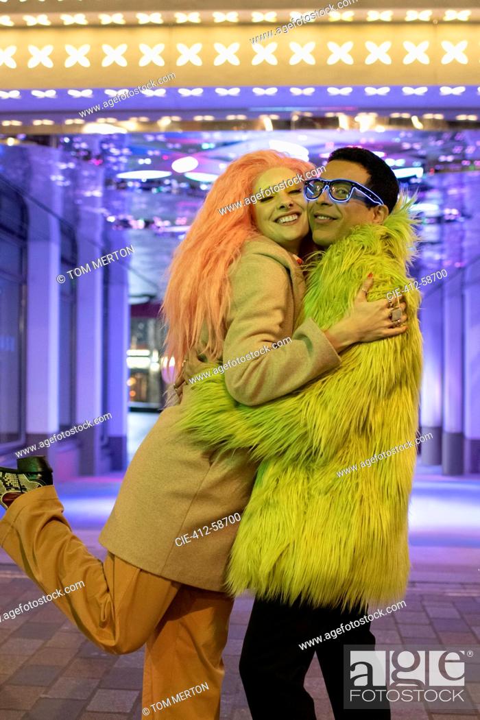 Imagen: Portrait happy stylish couple hugging under neon lights on sidewalk.