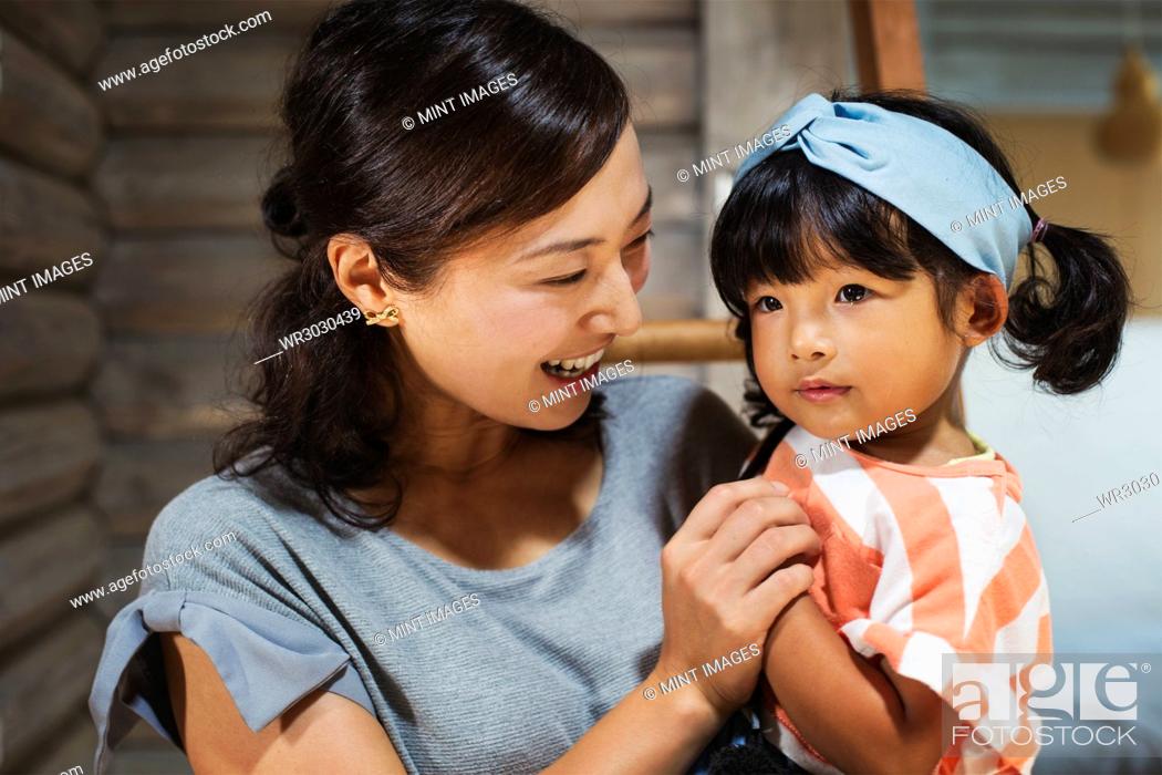 Stock Photo: Smiling woman holding young girl with black pigtails wearing blue hairband.