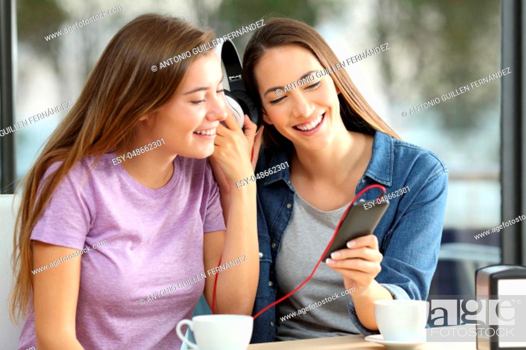 Stock Photo: Two happy friends sharing on line music sitting in a bar.