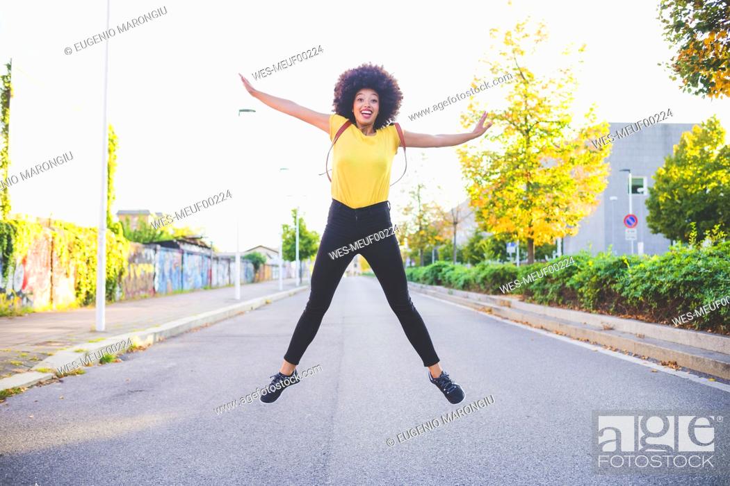 Stock Photo: Happy young woman with afro hairdo jumping on a street in the city.