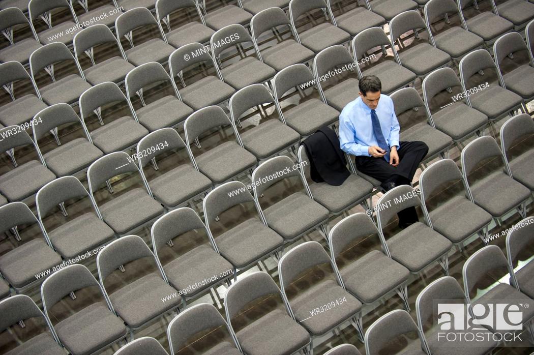 Stock Photo: View from above looking down on a businessman sitting alone in a room full of chairs prior to meeting in a conference centre.