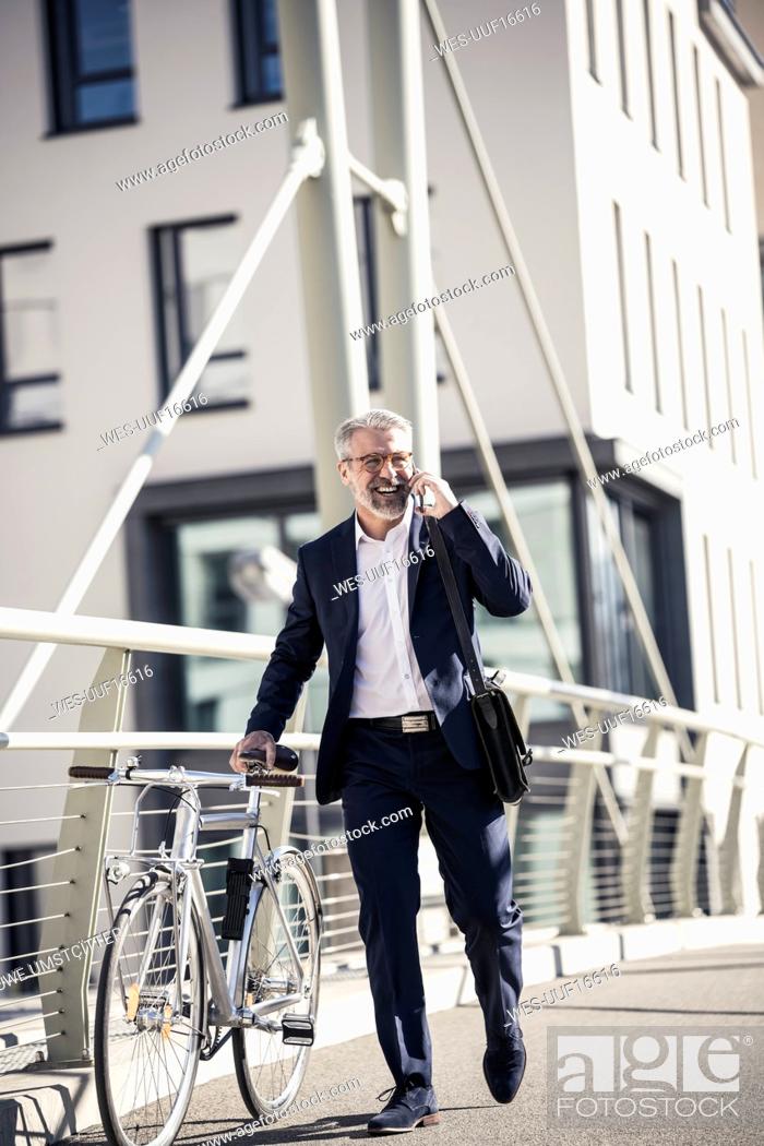 Stock Photo: Happy mature businessman with bicycle talking on cell phone in the city.
