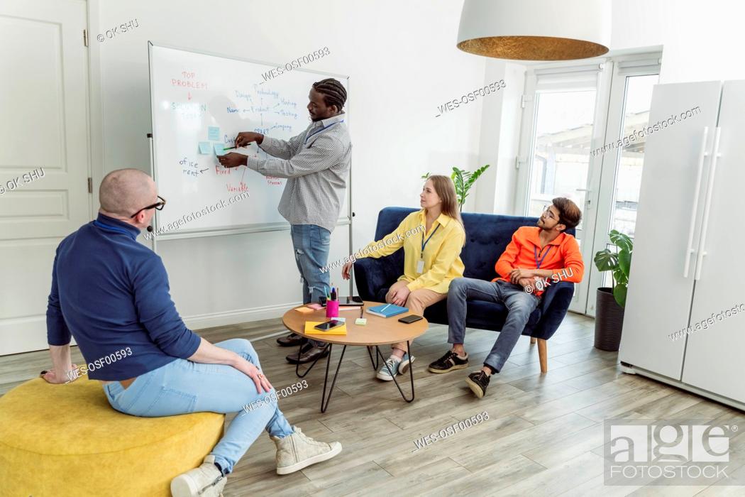 Stock Photo: Businessman pointing at adhesive note on whiteboard to colleagues in office.