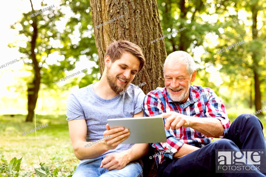 Stock Photo: Happy senior father sitting besides his adult son in a park looking at tablet.