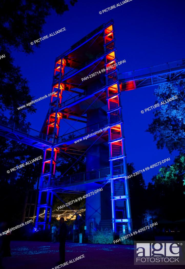 Stock Photo: 14 July 2023, Brandenburg, Beelitz: The observation tower on the grounds of the ""Baum & Zeit"" treetop trail in Beelitz-Heilstätten is illuminated in red in.